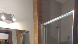 Un baño moderno con ducha envuelta en vidrio, lavamanos blanco y espejo.