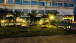 A multi-story building with balconies, a playground with swings and slides, and a parking area with a car. - Viola Beacon Resort Lonavala (Mawal)