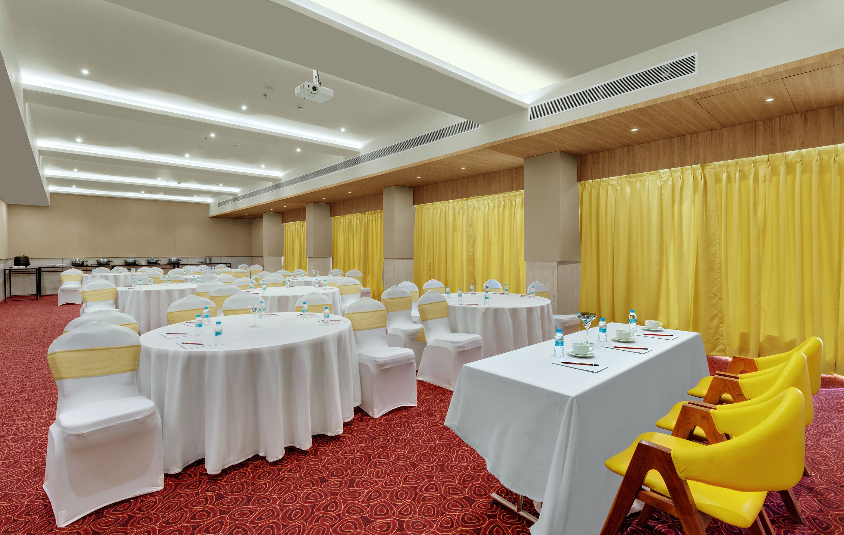 Un salón de conferencias con varias mesas redondas, manteles blancos y sillas amarillas.