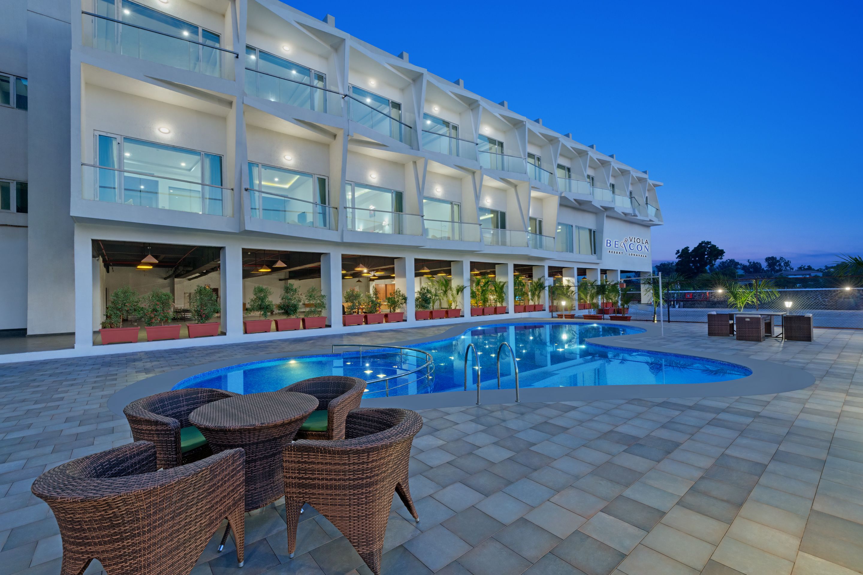 A hotel with a swimming pool, outdoor seating, and a well-lit facade.