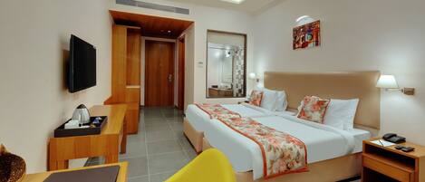 A hotel room with a bed, bedside table, lamp, TV, and a desk with a chair.