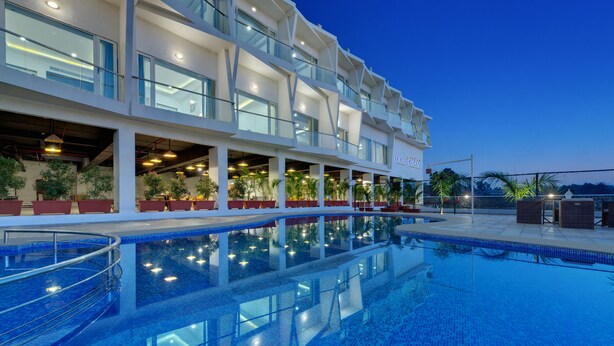 A hotel with a large outdoor swimming pool, multiple balconies, and indoor seating areas with potted plants. - Viola Beacon Resort Lonavala (Mawal)