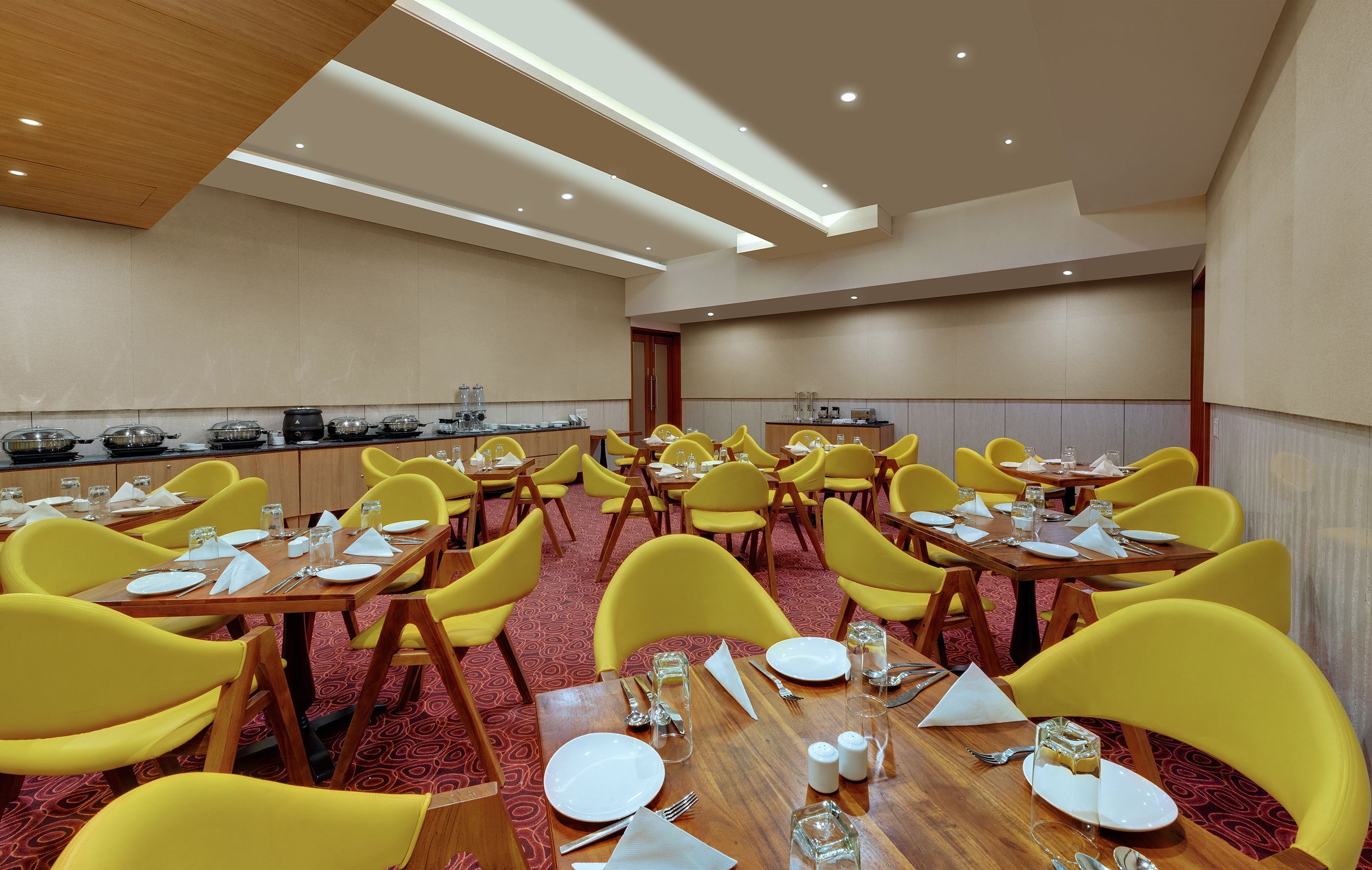 A hotel dining area with yellow chairs, wooden tables, and a red carpet.
