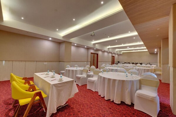 Uma sala de conferências com mesas redondas, cadeiras brancas e um tapete vermelho.
