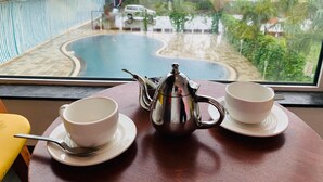 A table with a teapot, two cups, and a spoon, overlooking a swimming pool and lush greenery. - Viola Beacon Resort Lonavala (Mawal)