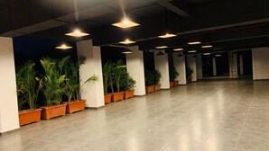A spacious indoor area with a tiled floor, multiple ceiling lights, and rows of potted plants along the walls. - Viola Beacon Resort Lonavala (Mawal)