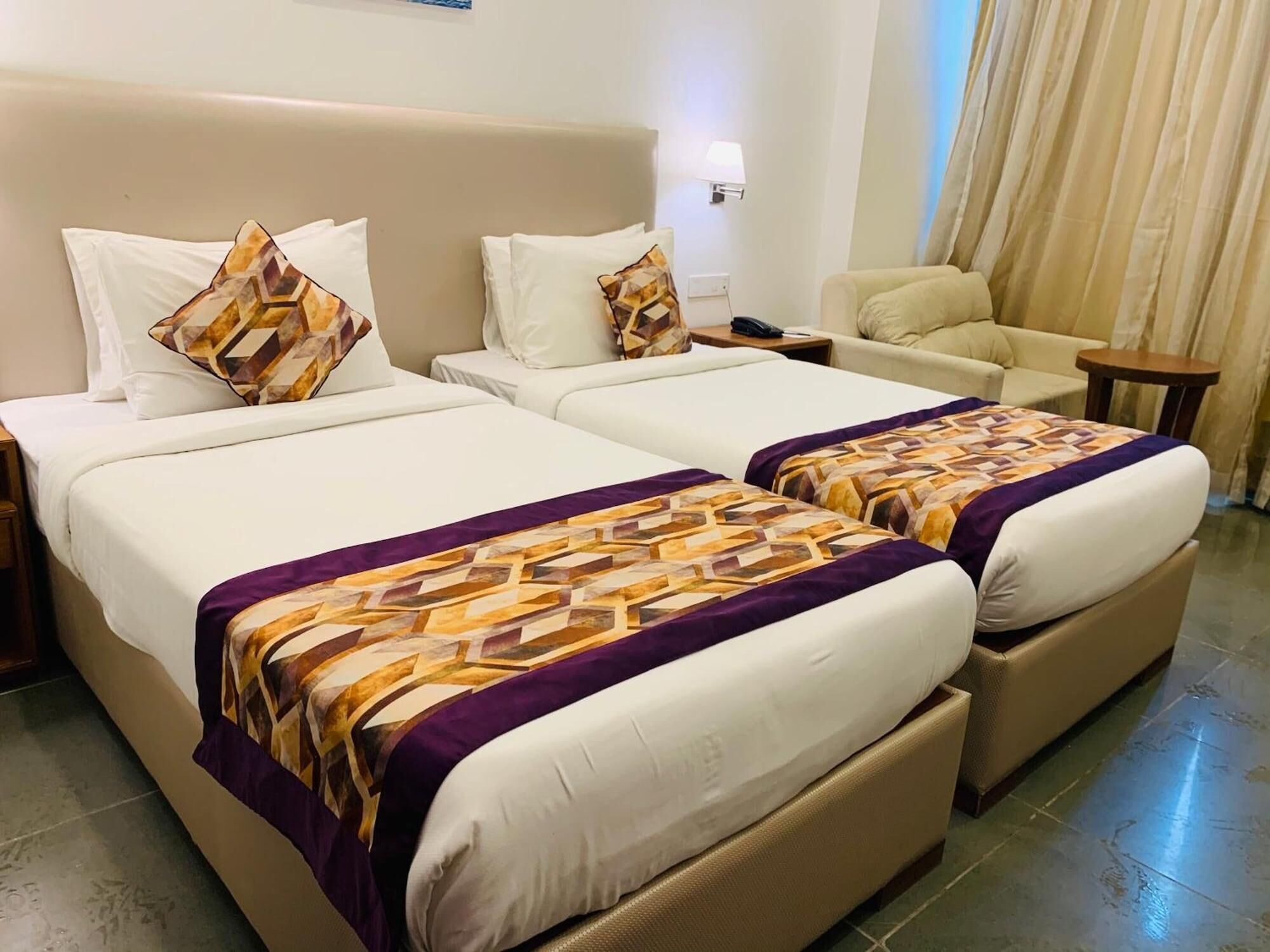 A hotel room with two beds, a sofa, a nightstand, and a lamp.
