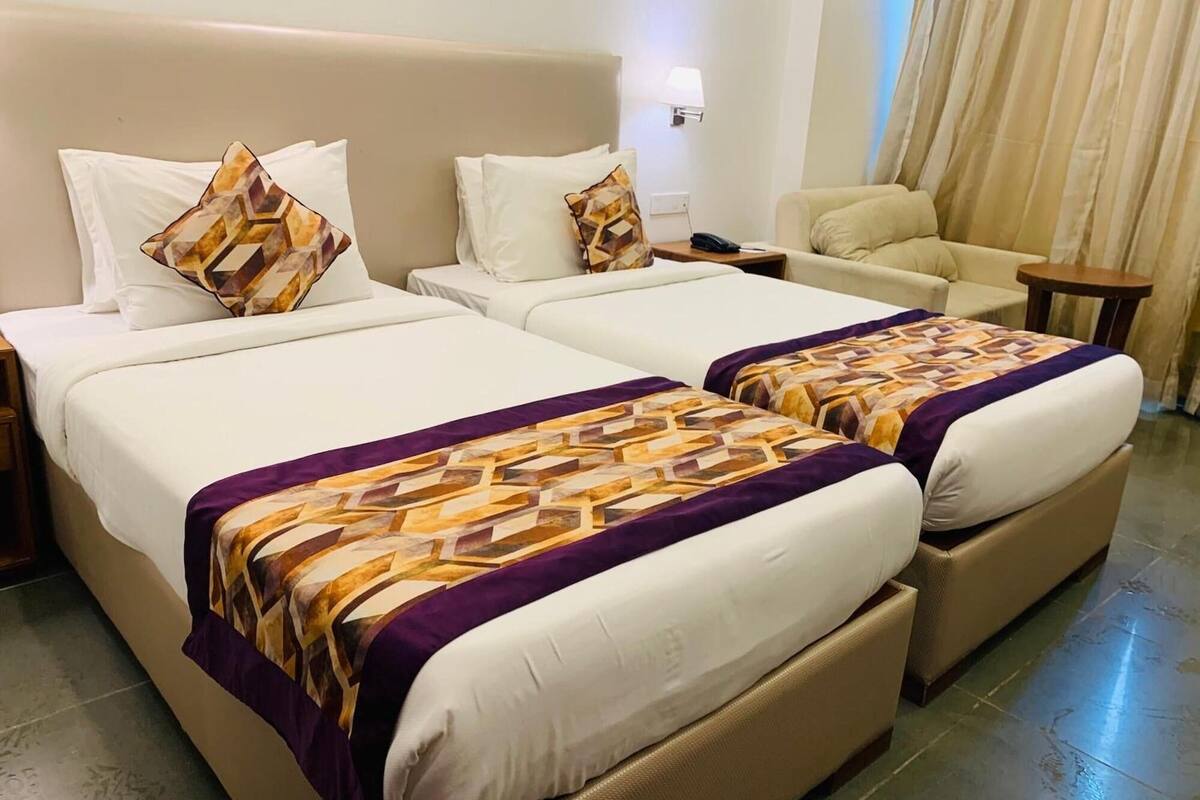 Une chambre d’hôtel avec deux lits, un canapé, une table de chevet et une lampe.