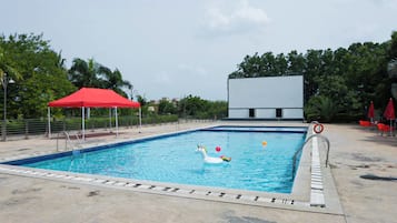 Ein Schwimmbecken mit einer roten Markise, ein weißes Gebäude im Hintergrund und ein klarer Himmel.
