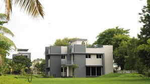 A modern two-story building with a flat roof, surrounded by a well-maintained lawn and palm trees.