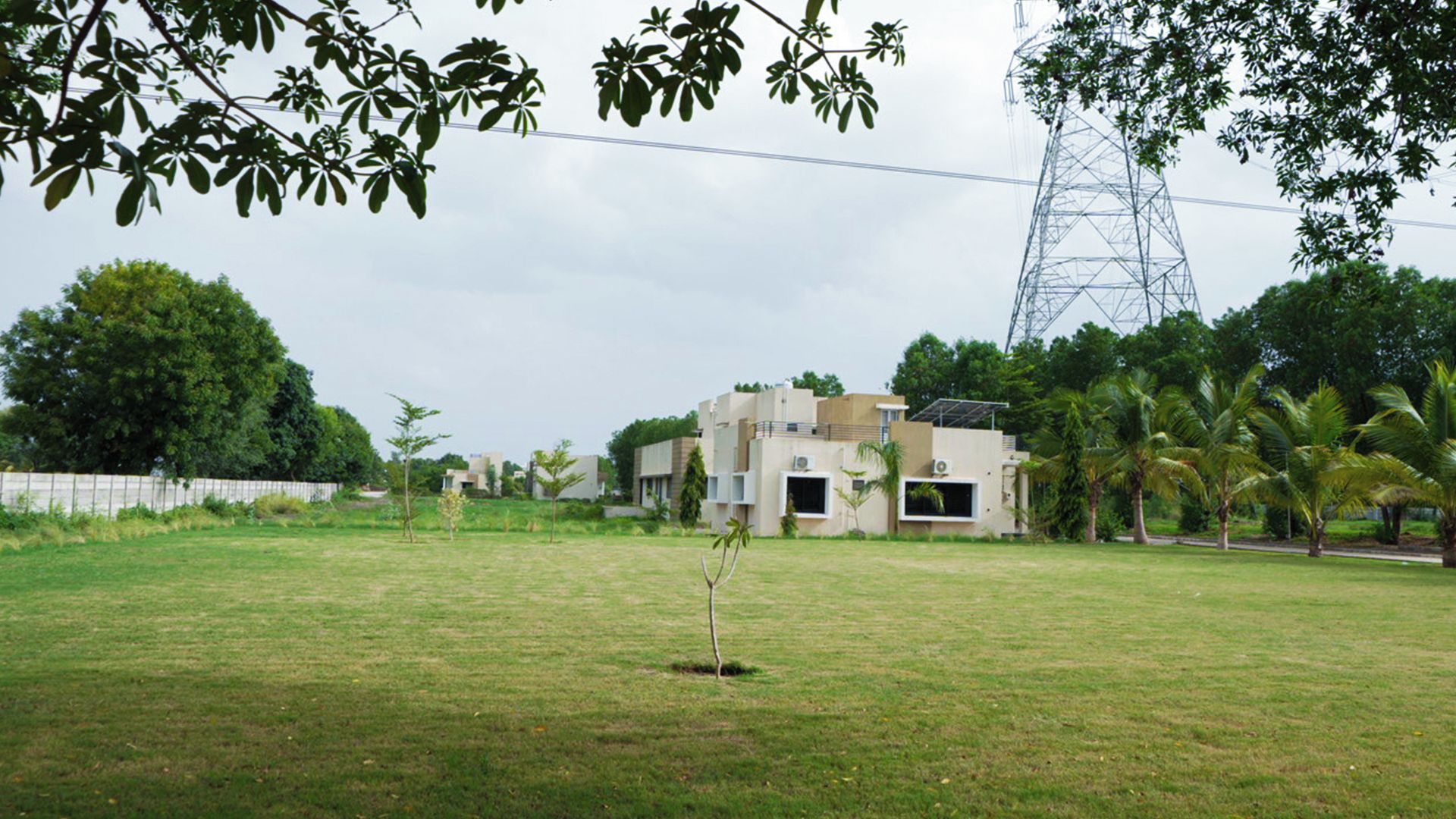 A residential area with a modern house, a grassy lawn, and a power line tower in the background.