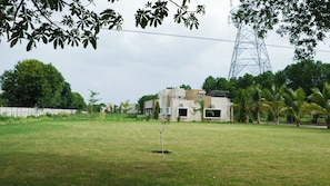 A residential area with a modern house, a grassy lawn, and a power line tower in the background. - Malhaar Resort (Dahegam)