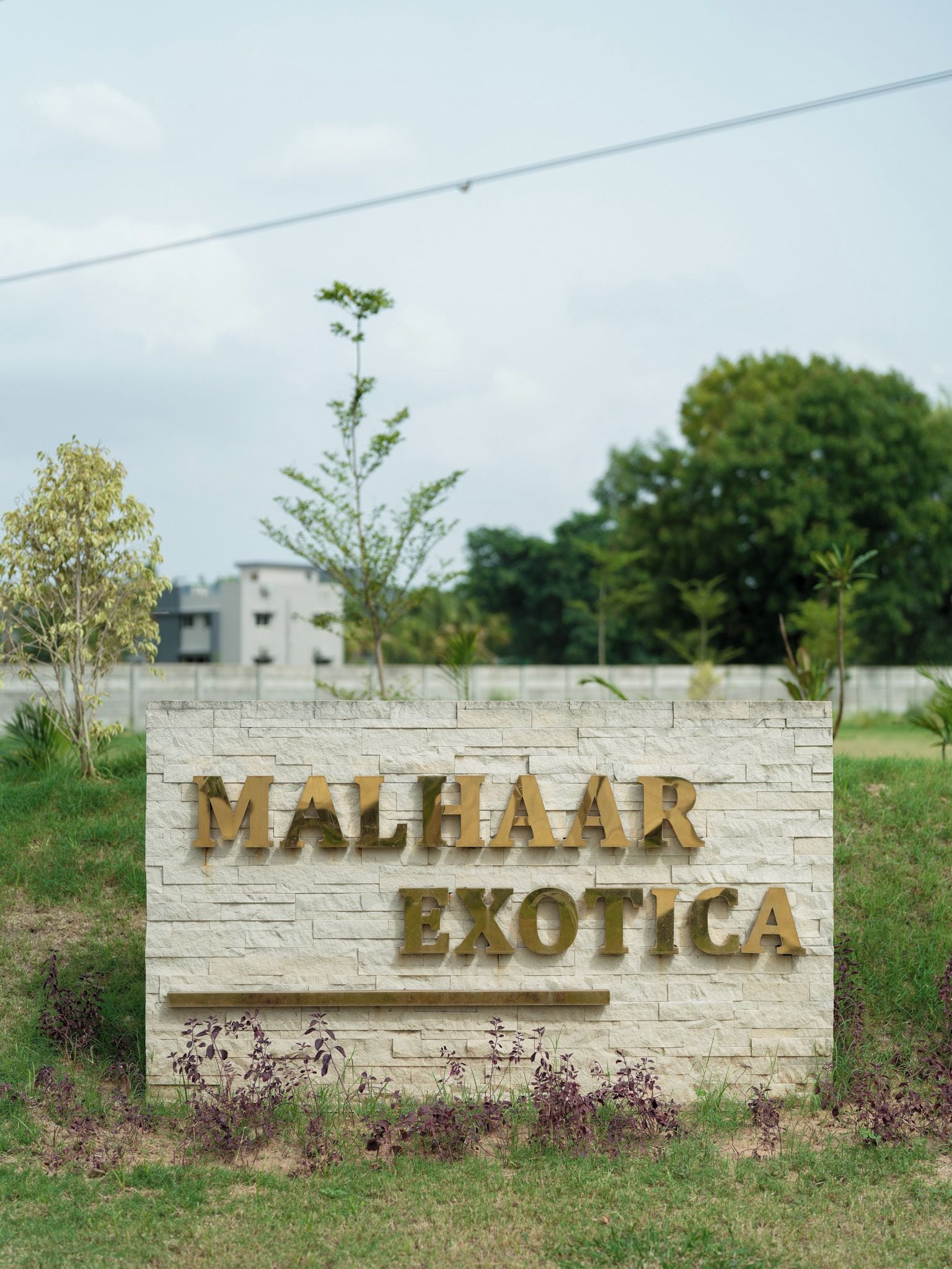 Een bordje voor 'MALHAAR EXOTICA' met een stenen muur op de achtergrond en wat groen eromheen.