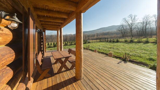 Una terraza de madera con mesas de picnic y vistas a un campo verde y montañas al fondo.
