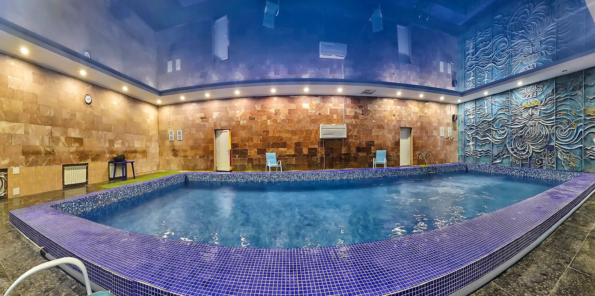 A large indoor swimming pool with a tiled edge, surrounded by stone walls and a decorative mural.
