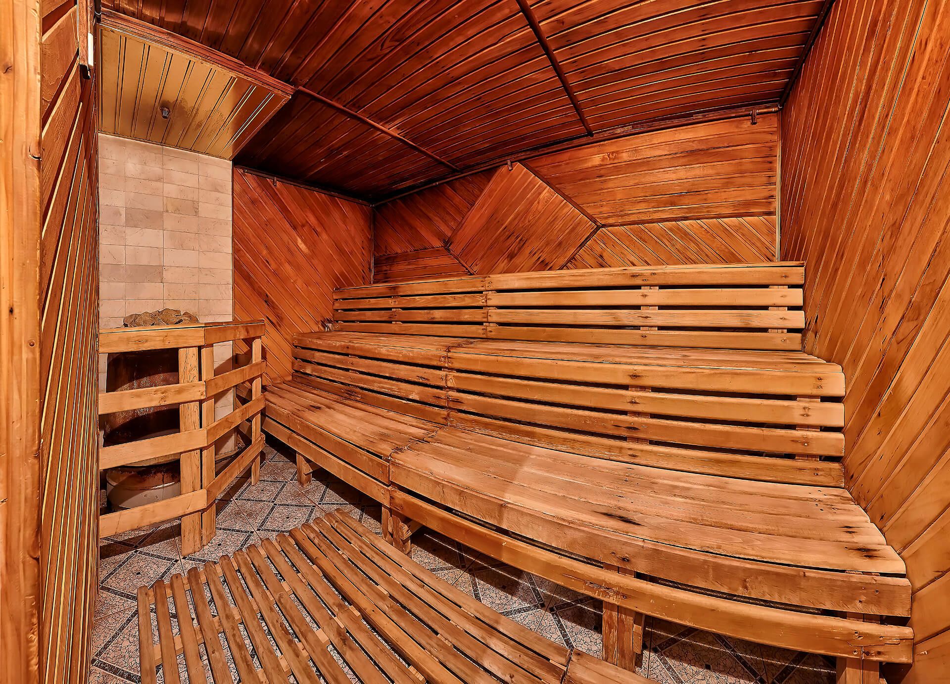 Una sauna con bancos de madera dispuestos en forma semicircular, una mesa de vidrio y suelo de baldosas.