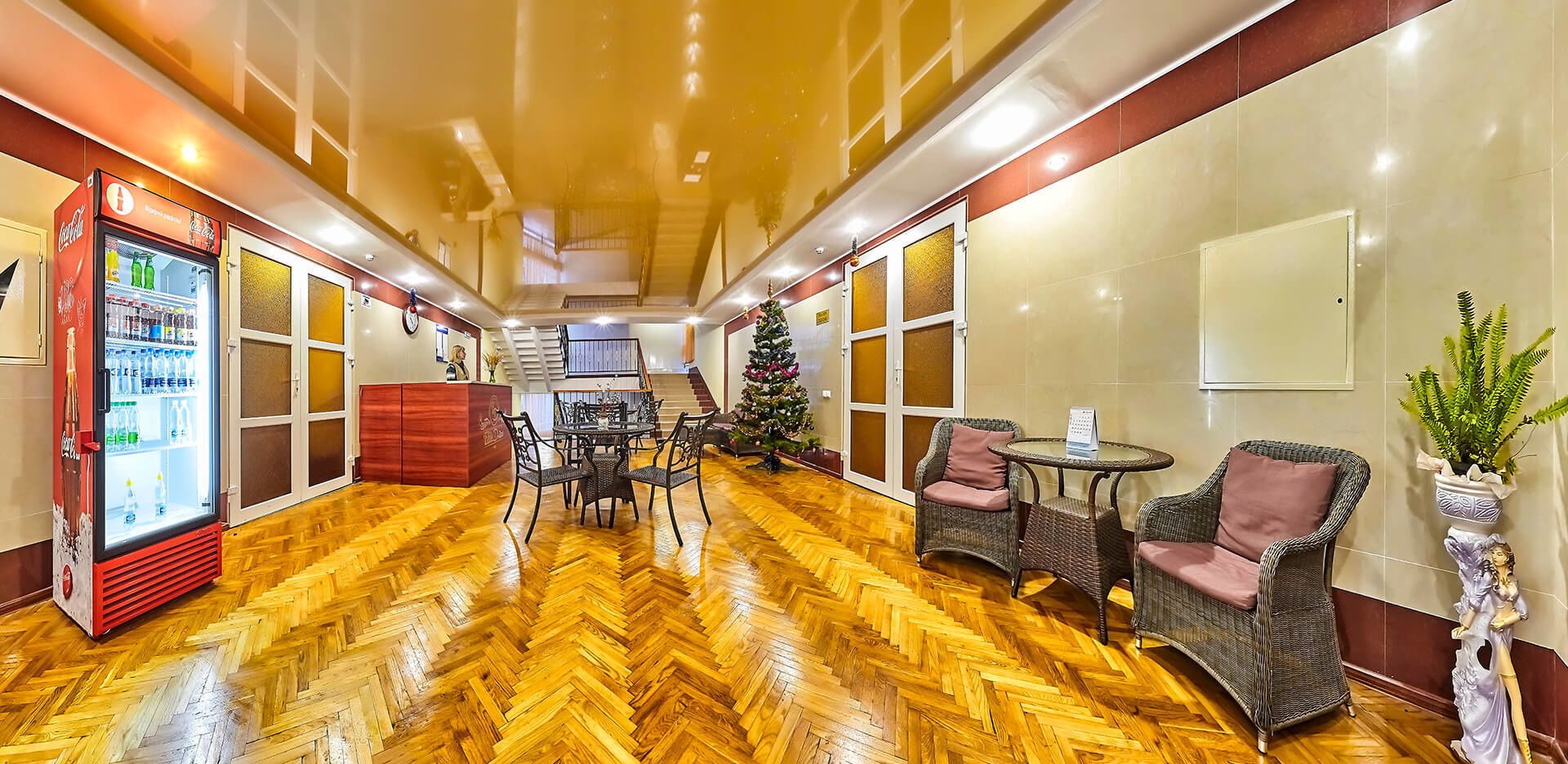 A hotel lobby with a herringbone wooden floor, a Coca-Cola refrigerator, a Christmas tree, wicker chairs, and a reception desk.