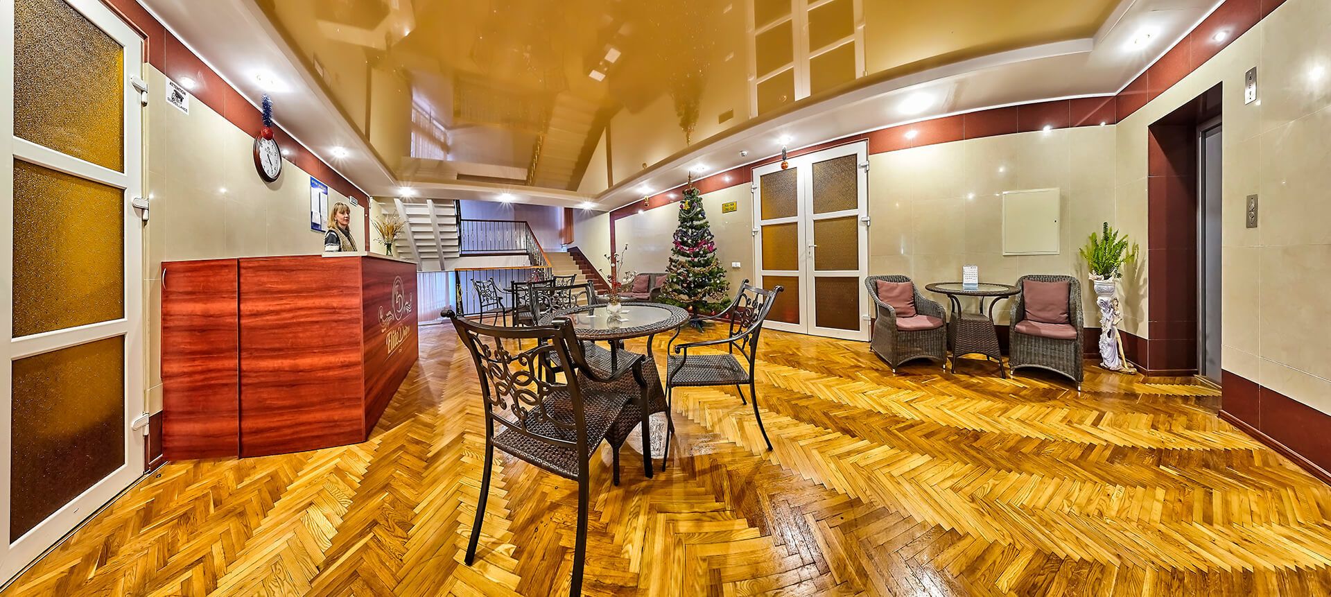 A hotel lobby with a wooden herringbone floor, a reception desk, a Christmas tree, and wicker chairs.
