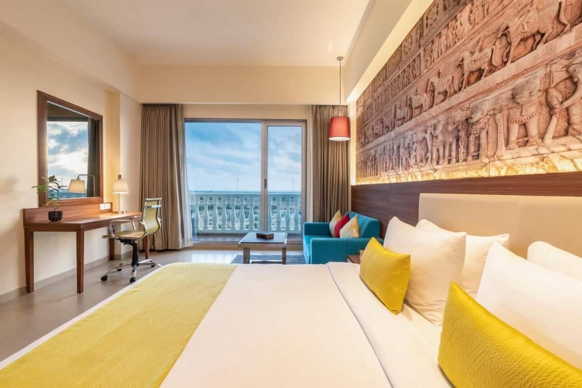 A hotel room with a bed, a desk, a chair, a sofa, a view of the sea, and a decorative wall.