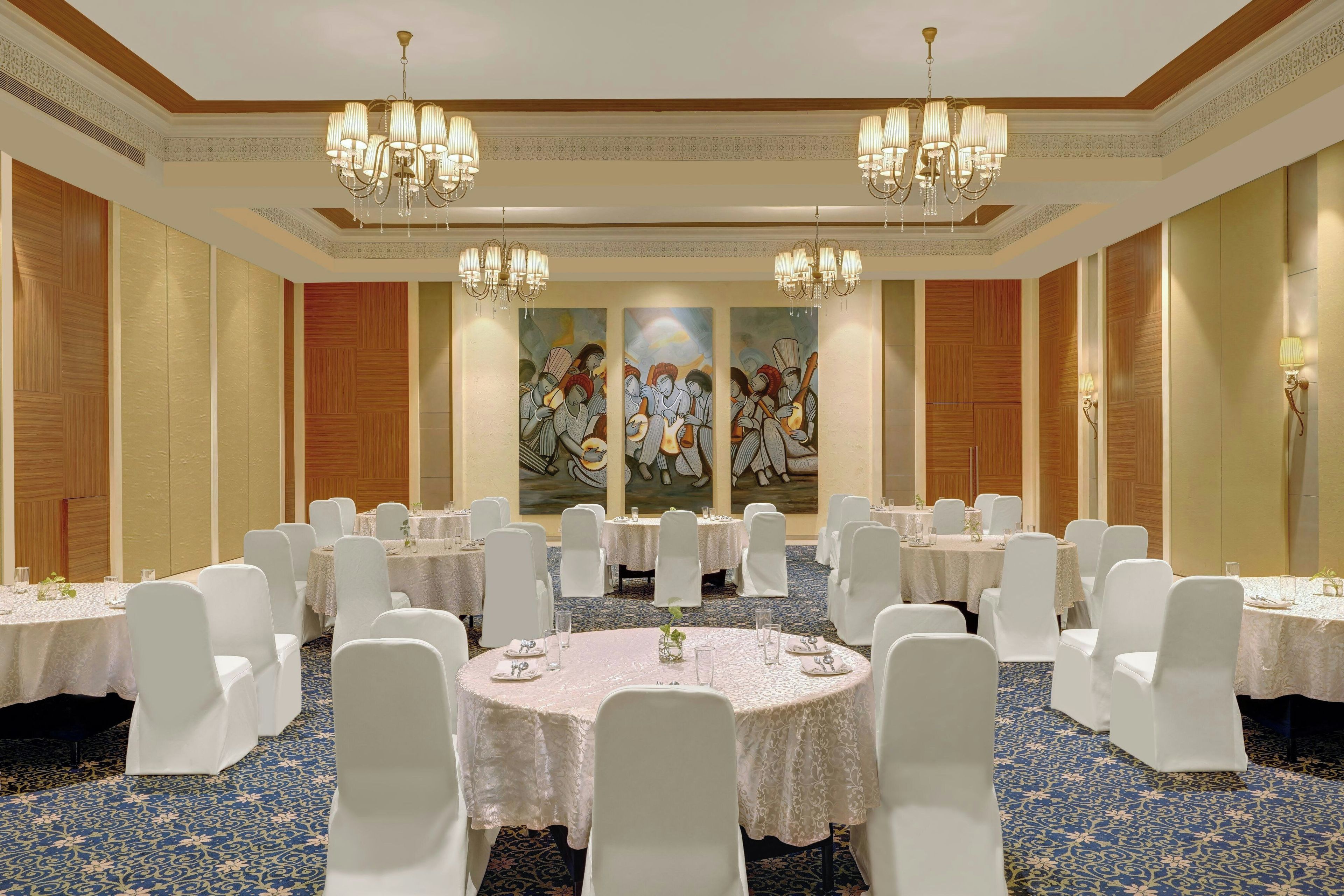 A banquet hall with round tables, white chairs, and chandeliers.