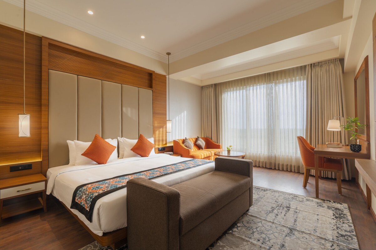 A modern hotel room with a large bed, a sofa, a desk, and a window with curtains.