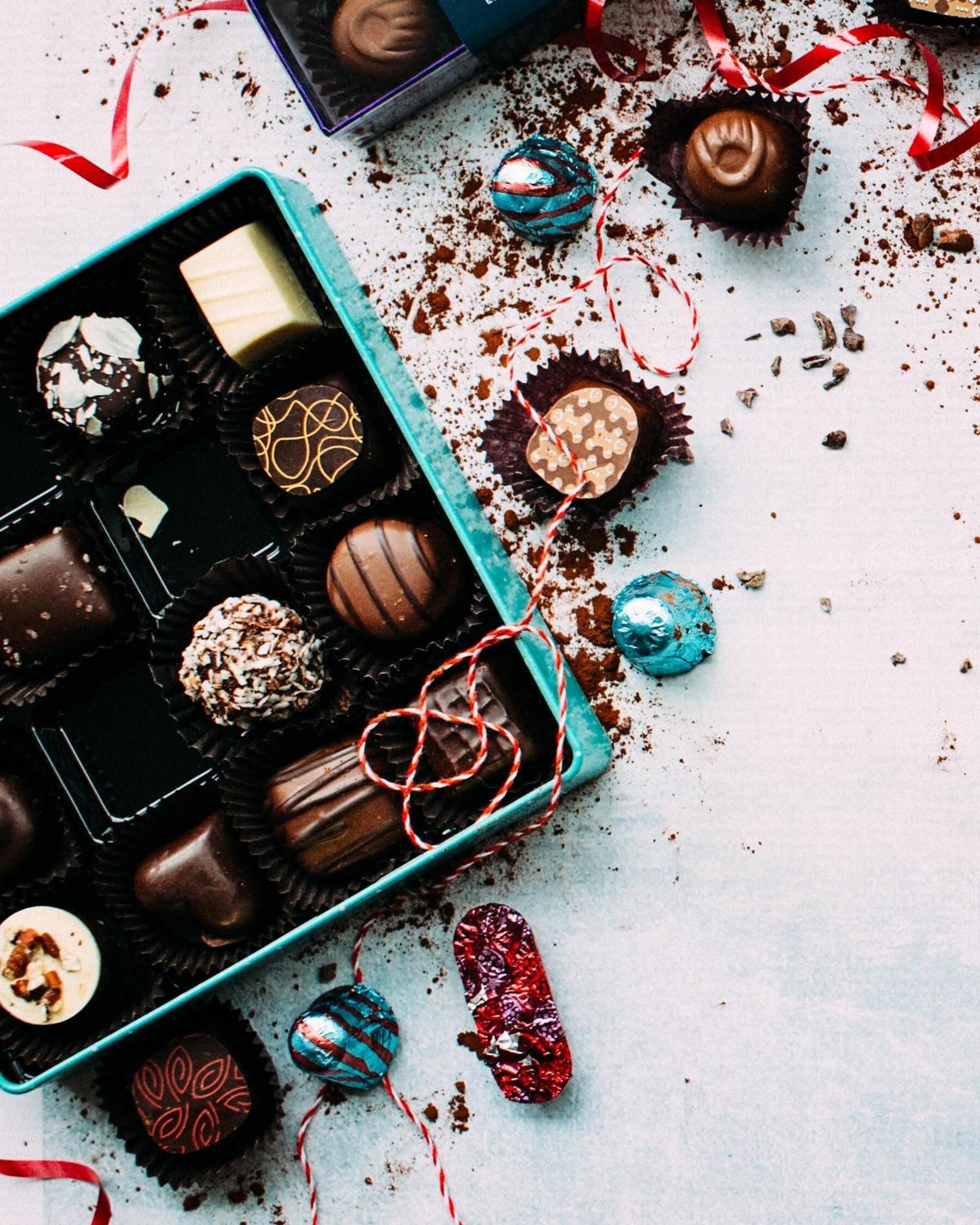 A variety of chocolates in a teal box with some scattered around.
