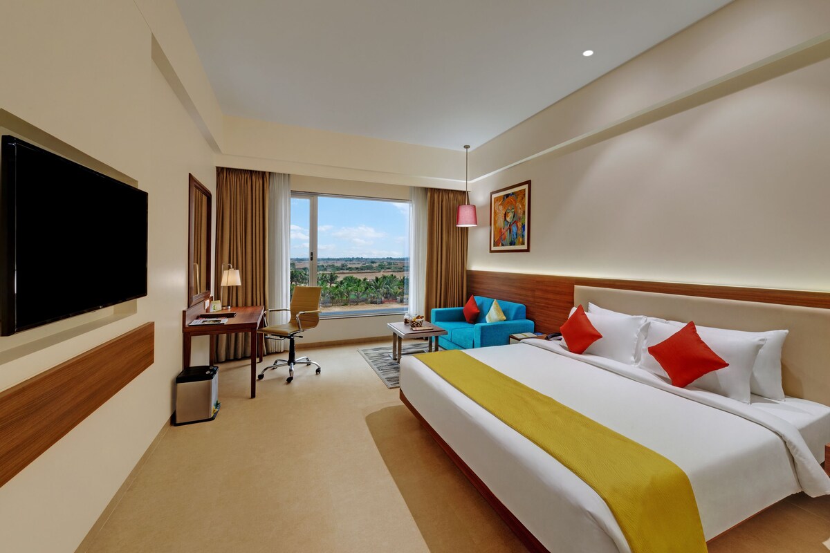 A hotel room with a large bed, a desk with a chair, a television, and a view of the outdoors.