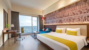 A hotel room with a large bed, a sofa, a desk, and a balcony with a view.
