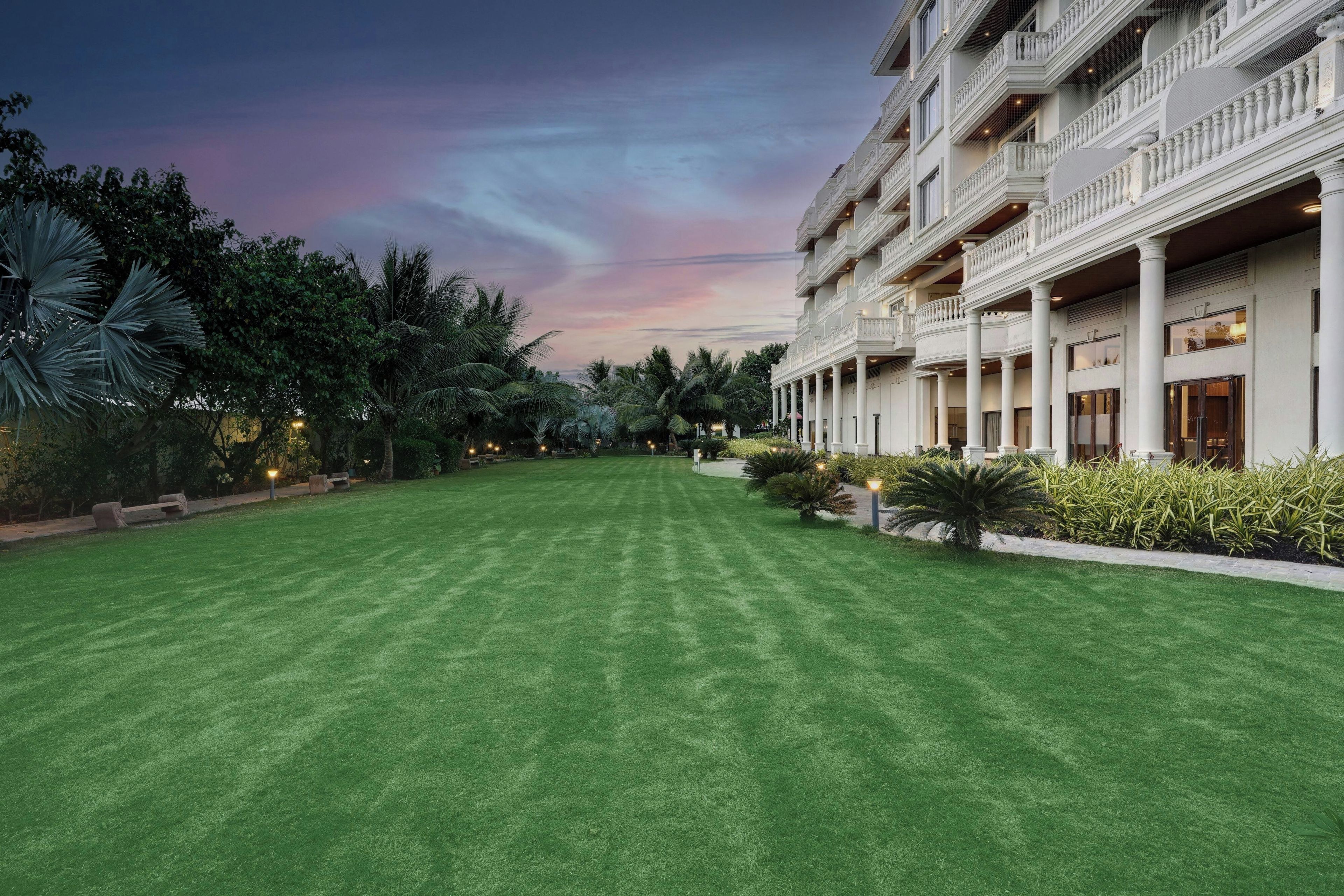A hotel with a well-maintained lawn, multiple balconies, and lush greenery.