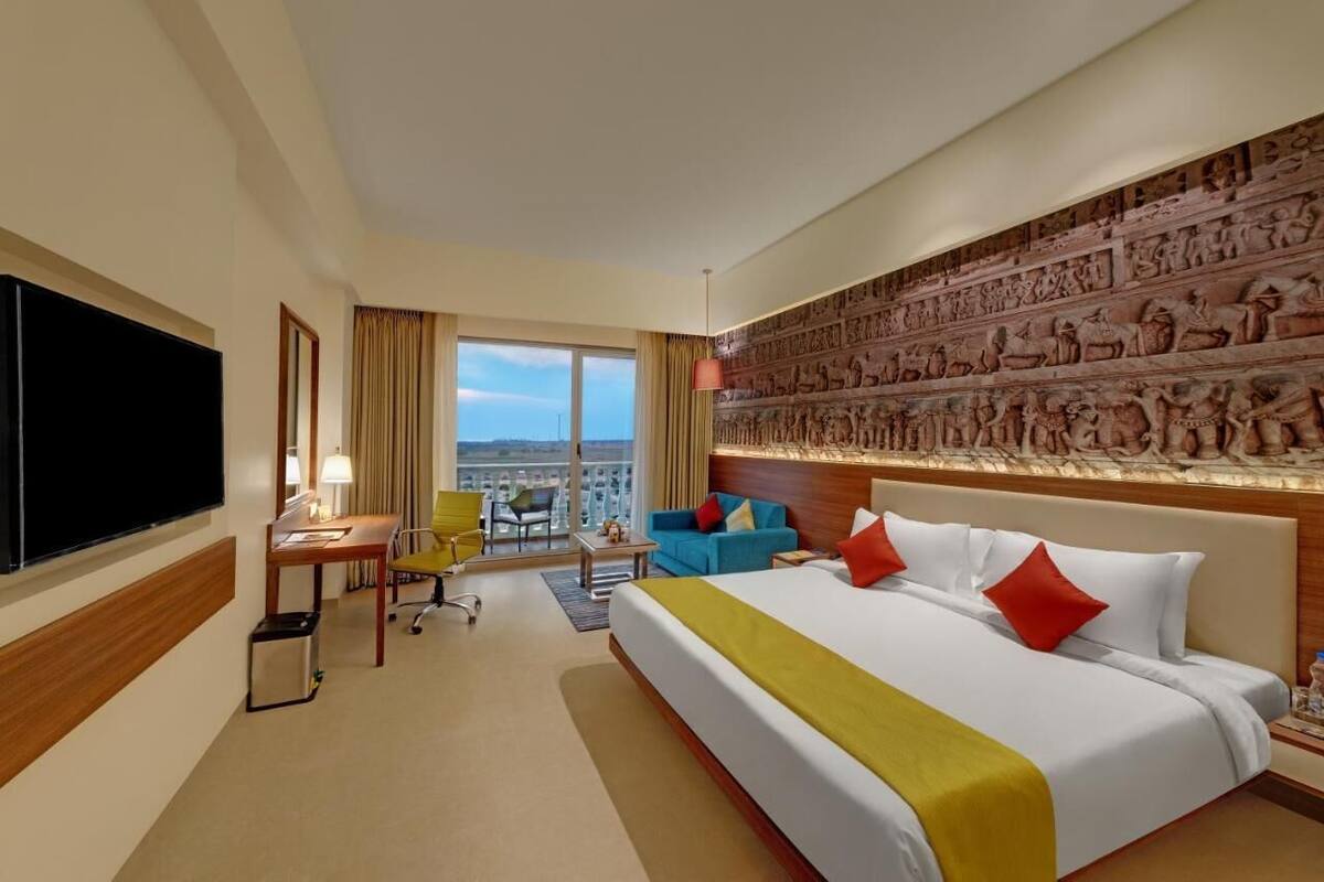 A hotel room with a large bed, a desk, a chair, a sofa, and a wall with ancient carvings.