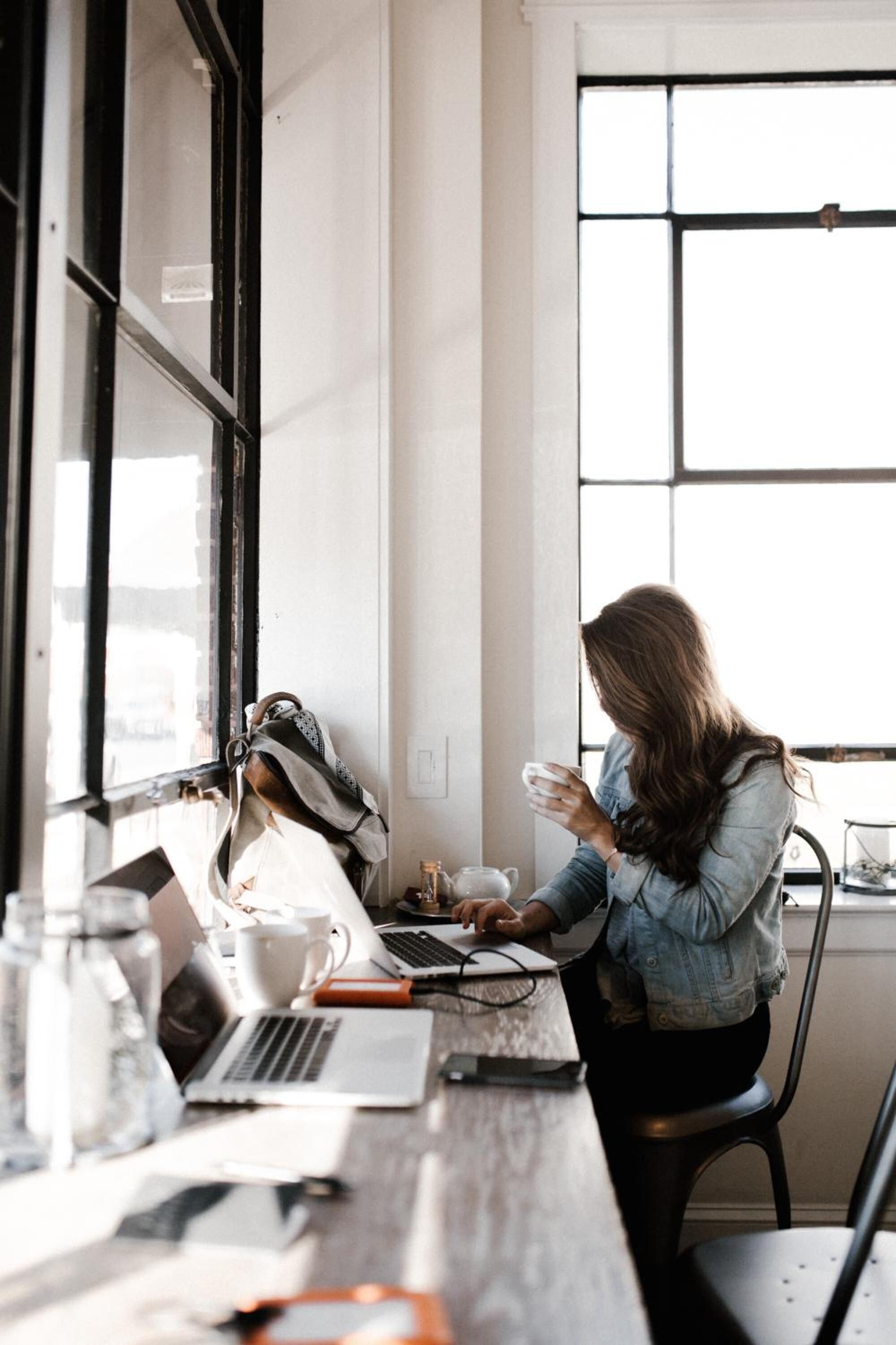 A person working at a desk with a laptop, a cup, and a notebook.