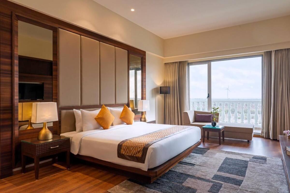 A hotel room with a large bed, a TV, a desk with a lamp, a chair, and a balcony with a view.