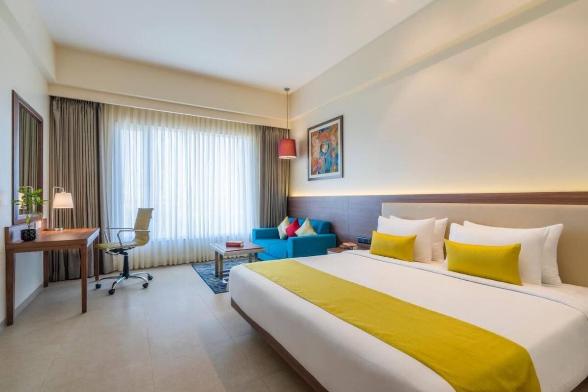 A hotel room with a large bed, a desk, a chair, a sofa, and a window with curtains.