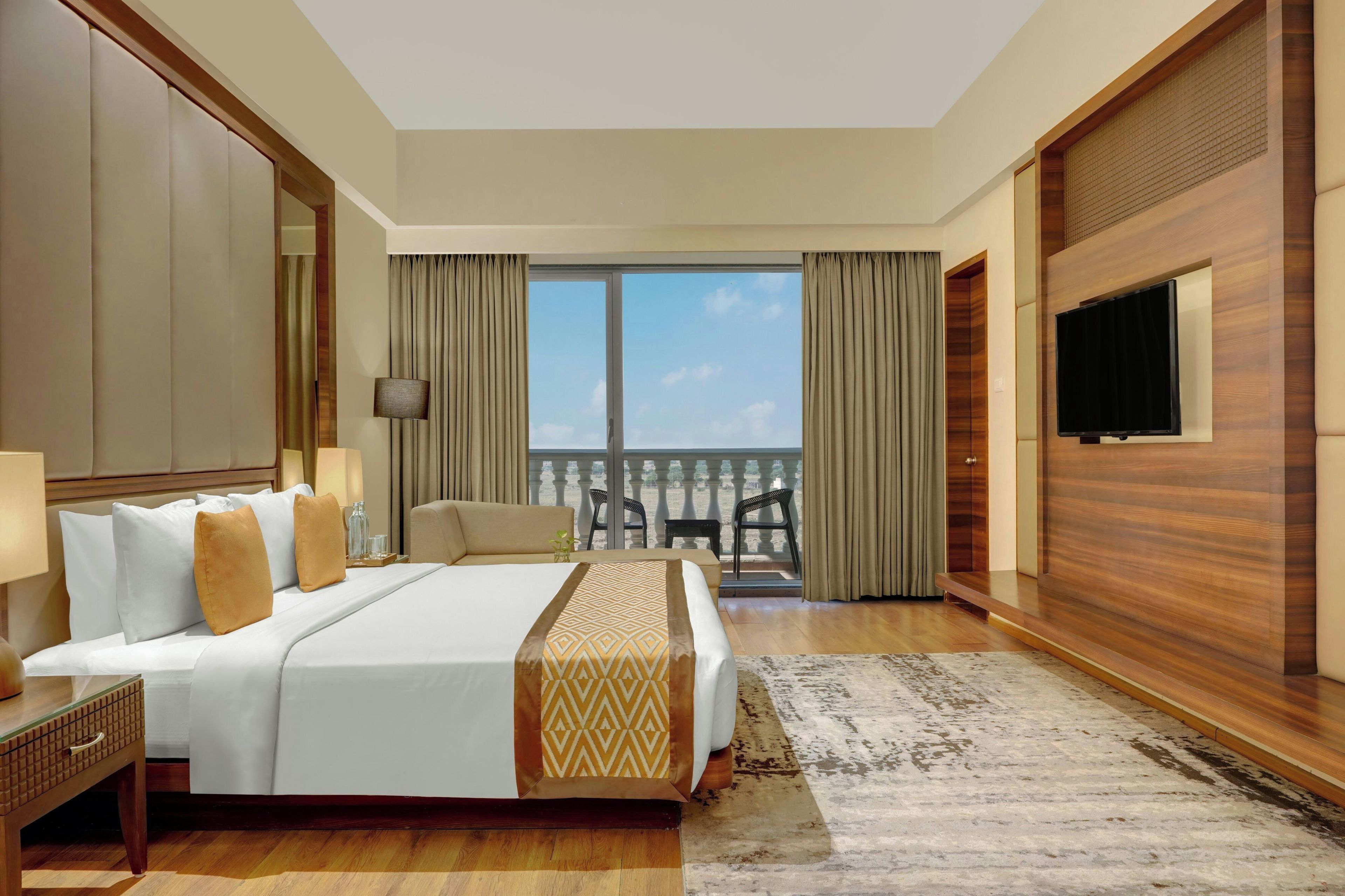 A hotel room with a large bed, a TV, a balcony with a view, and a wooden accent wall.