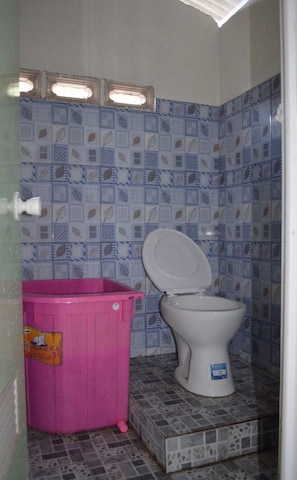 Un baño con inodoro, un cubo de basura rosa y baldosas estampadas en las paredes y el piso.