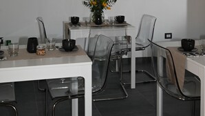 A modern dining area with a white table, clear chairs, and geometric pendant lights. - B&B Palummelle (Naples)