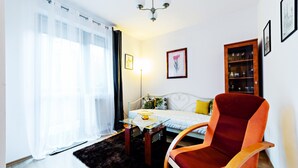 Una sala de estar acogedora con un sofá, un sillón rojo, una mesa de centro de vidrio y una estantería.