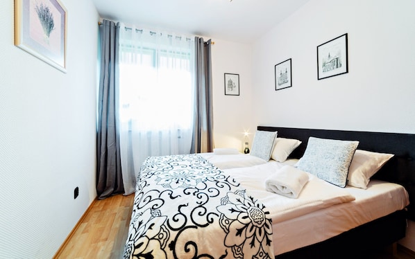A bedroom with a bed, curtains, and framed pictures on the wall.