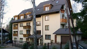 Un edificio residencial de varios pisos con balcones, un camino de entrada cerrado y una zona de estacionamiento pequeña.