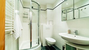 Un baño moderno con ducha de mampara de vidrio, inodoro blanco y lavamanos con espejo.