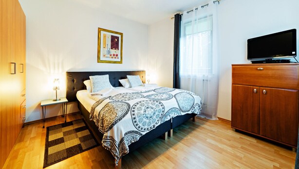 Un dormitorio ordenado con cama, mesitas de noche, televisor y armario.