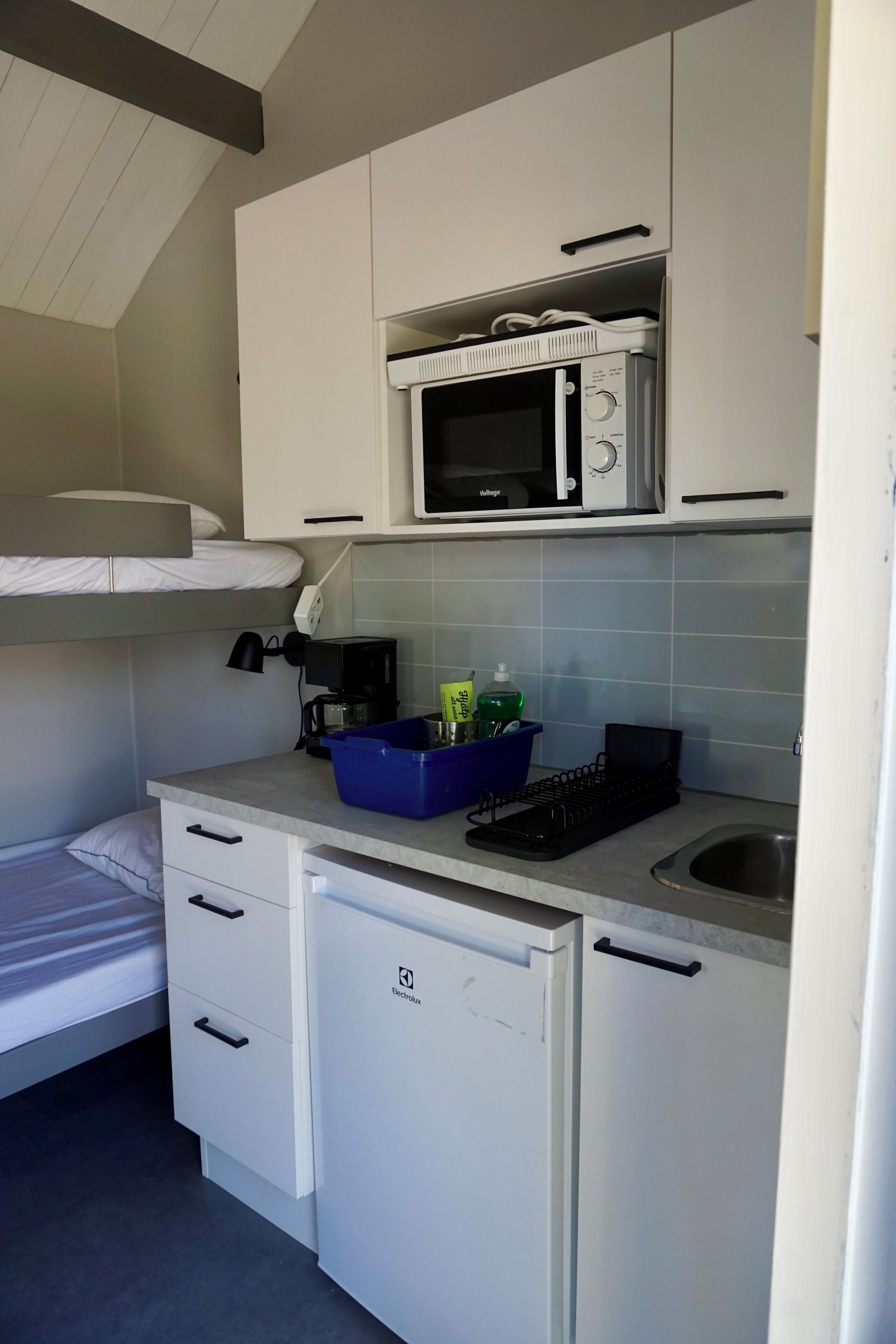 Une petite cuisine équipée comprenant un four à micro-ondes, un petit réfrigérateur, un évier et un plan de travail avec un égouttoir bleu.