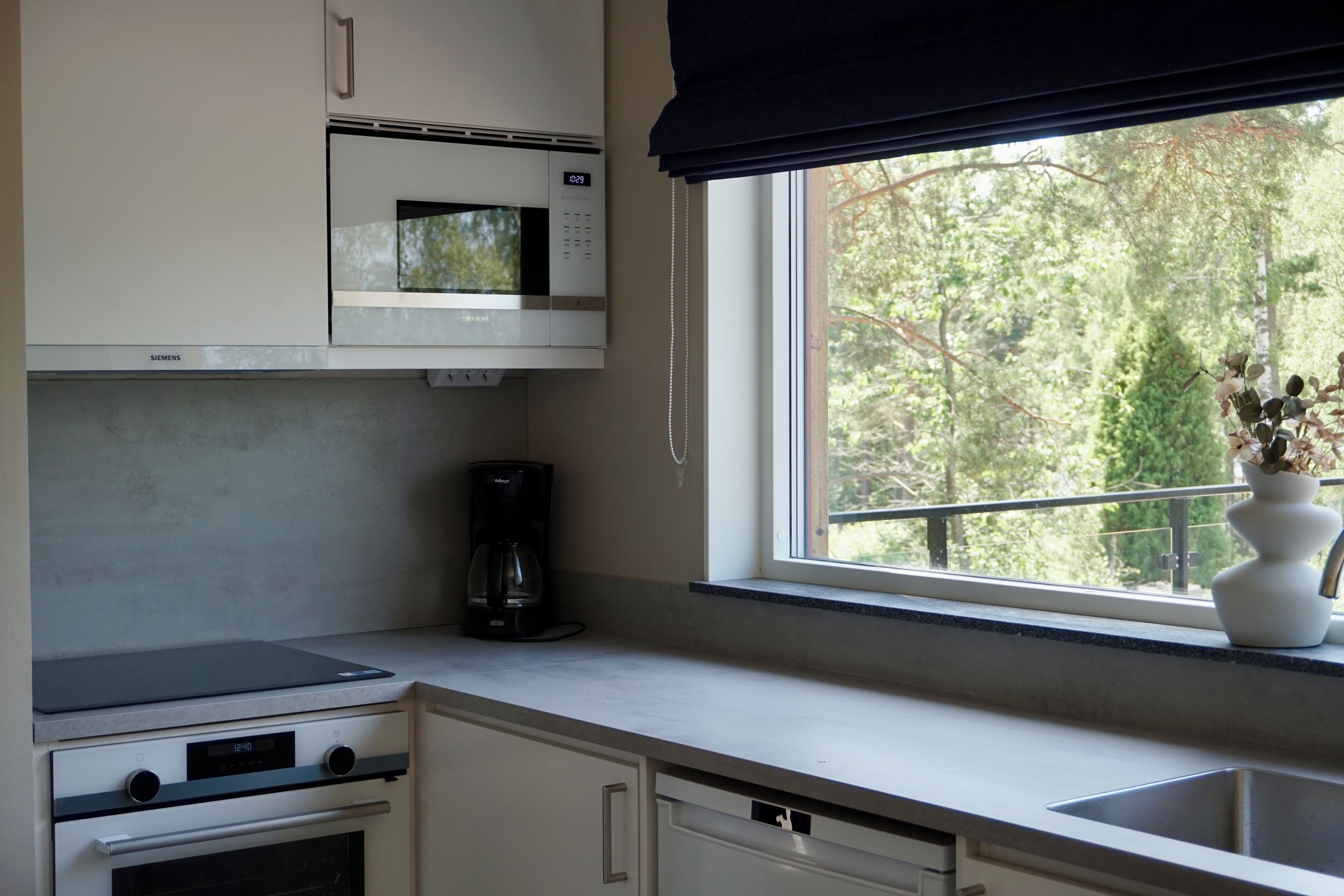 Eine Küche mit Mikrowelle, Kaffeemaschine und einem Fenster mit Blick auf Bäume.