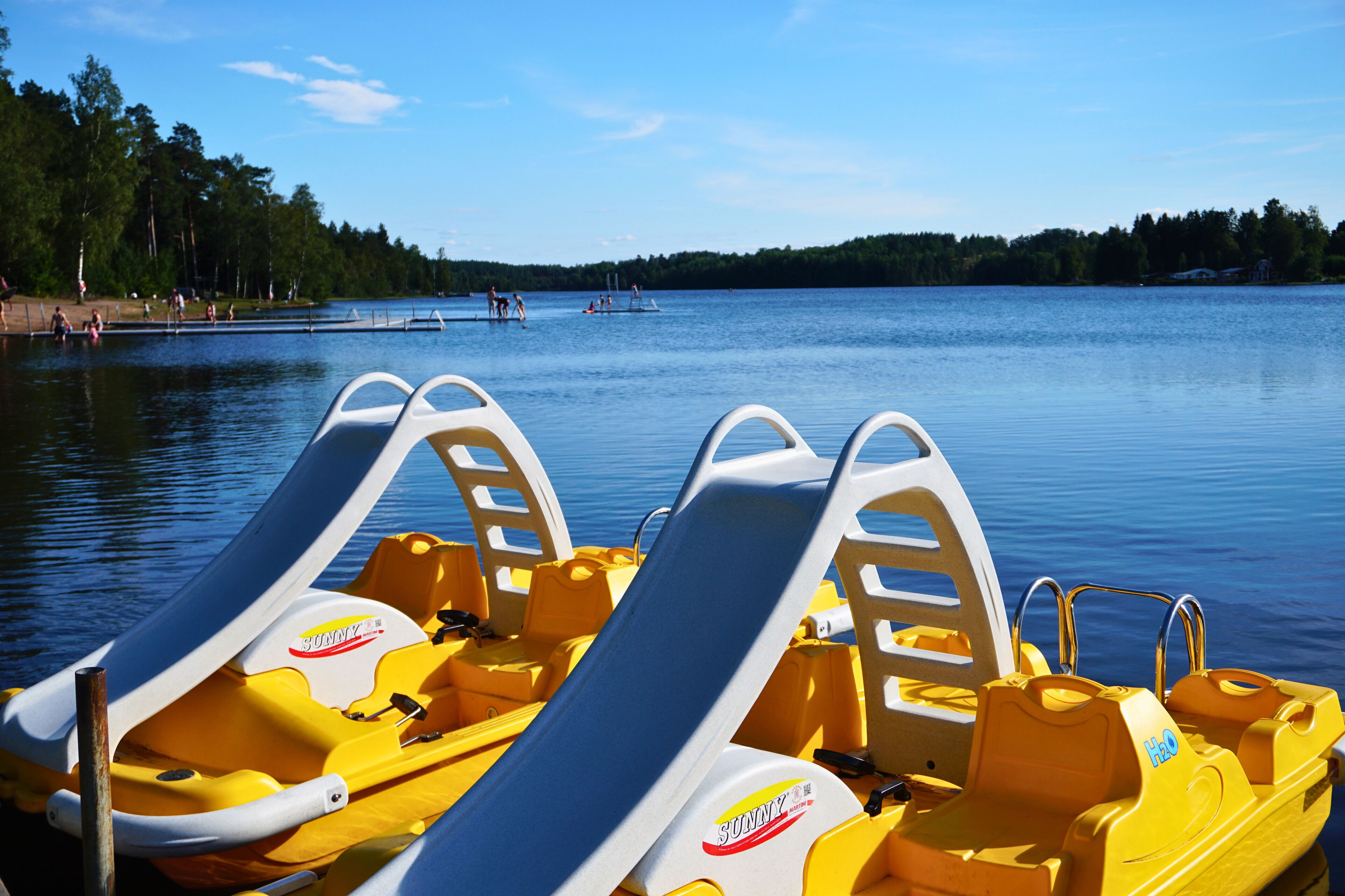A row of yellow inflatable boats with white seats and a 'Sunny' logo, docked at a calm lake with a clear sky.