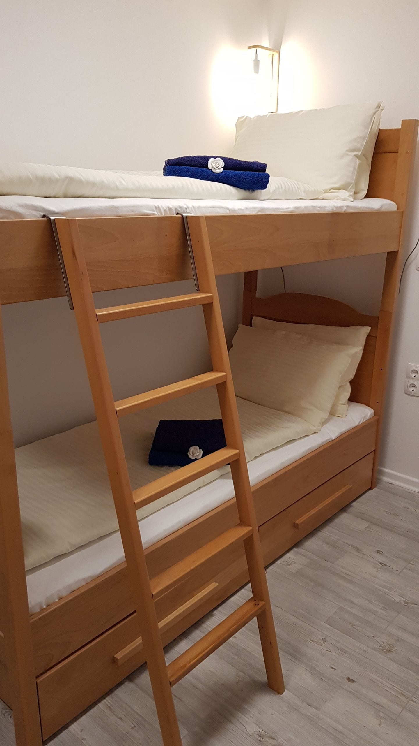 A bunk bed with a wooden ladder, a bedside table, and a wall-mounted light fixture.