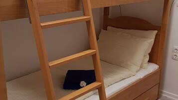 A bunk bed with a wooden ladder, a bedside table, and a wall-mounted light fixture.