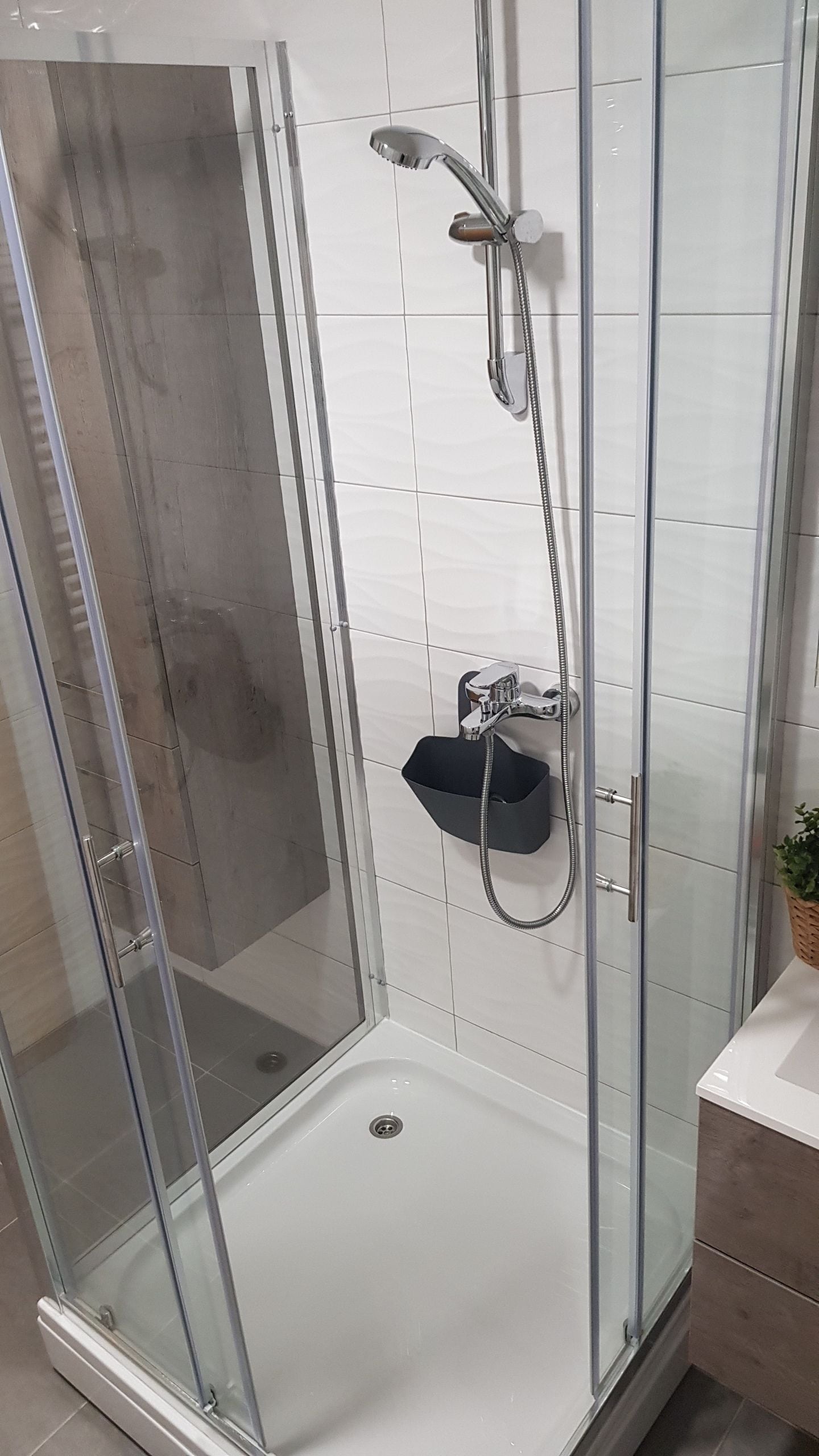 Eine Duschkabine mit Glaswänden, einer Handbrause und einem am Wand montierten Wasserhahn.
