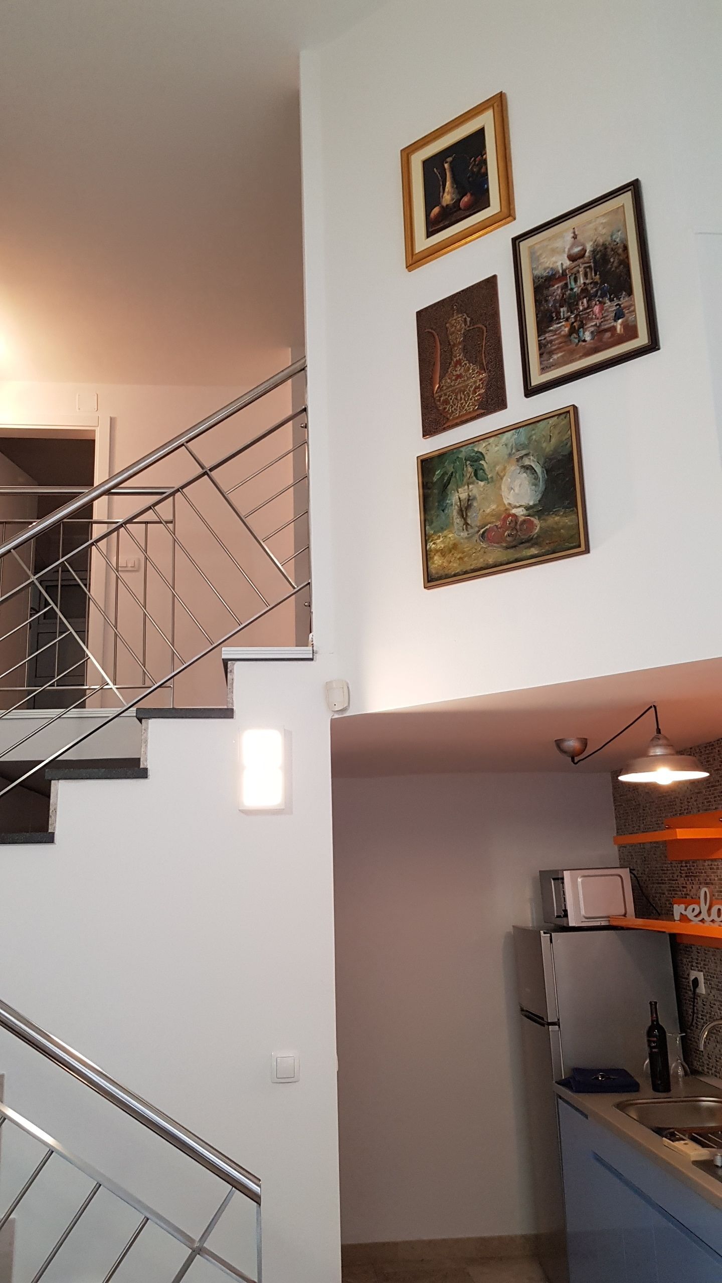 A staircase with a metal railing leading to an upper floor. There are four framed artworks on the wall above the staircase.