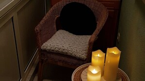A corner room with a wicker chair, a small table with candles, and a potted plant. - Galeria Nura (Mostar)