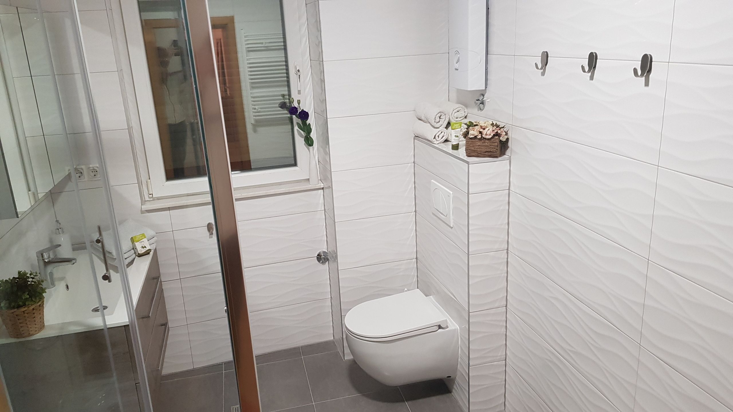 A small bathroom with white tiles, a toilet, a sink, and a shower area.